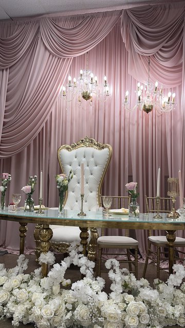 A gold and ivory throne chair framed by a cloud of white flowers against blush draping