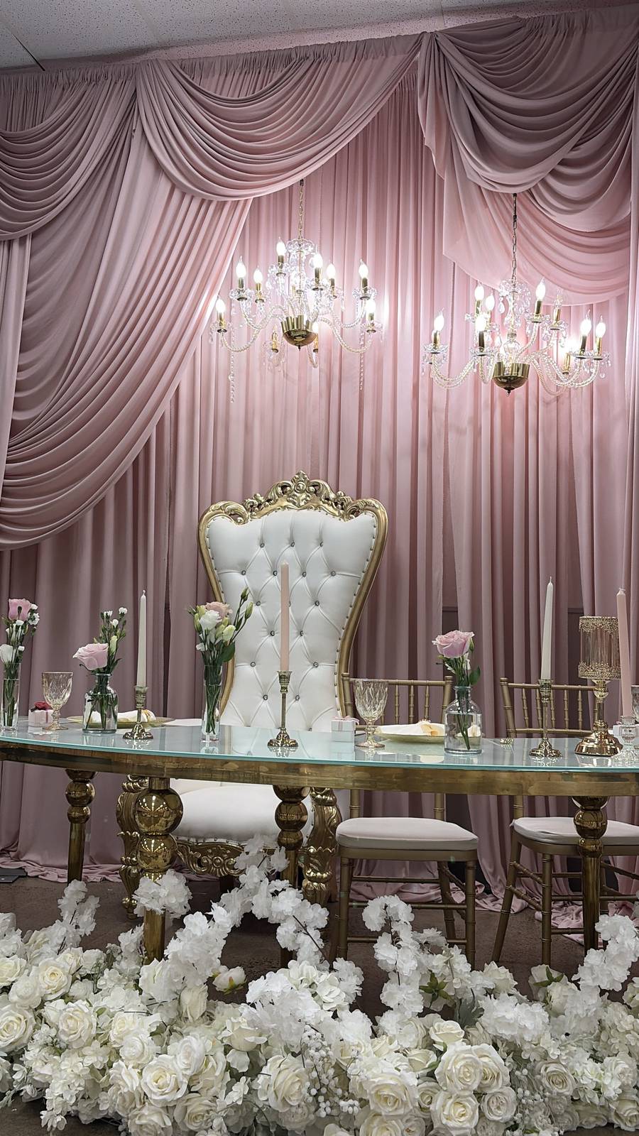 A gold and ivory throne chair framed by a cloud of white flowers against blush draping
