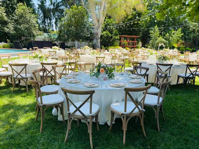 Round garden tables in ivory linen with cross-back chairs and peach centerpieces