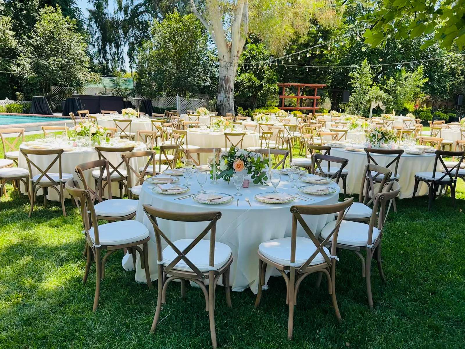 Round garden tables in ivory linen with cross-back chairs and peach centerpieces