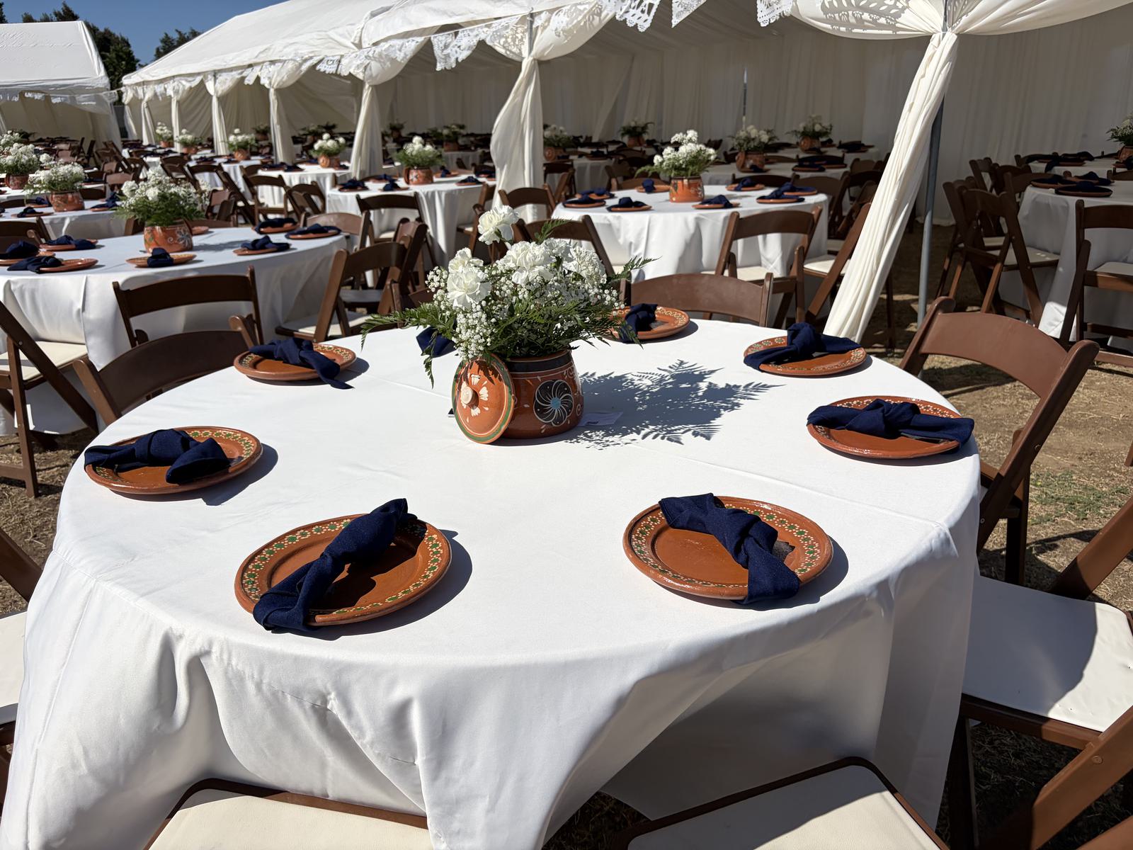 A round table in white linen set with hand-painted terracotta chargers and navy napkins